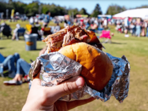 a barbecue sandwich in the foreground, food truck festival in background