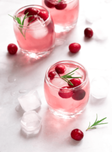 A pink seasonal drink with cranberries and rosemary as garnish
