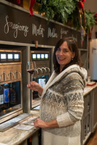 Michelle holding a glass of red wine by the wine dispensing stations