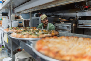 Jeremy behind the pizza counter, with pizzas in foreground