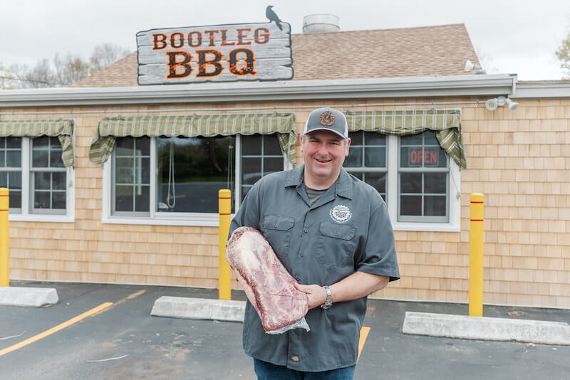 Fred, standing with a brisket, in front of Bootleg BBQ