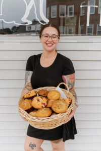Joni, outside her cafe, holding a basket of pastries and muffins