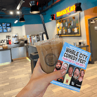 A hand with an iced coffee and a Whale City Comedy Fest brochure