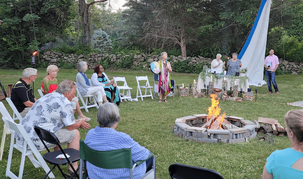 People gathered around a fire pit, one person holding a gong