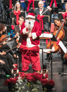 Yaniv Dinur dressed up as Santa, with the symphony behind him