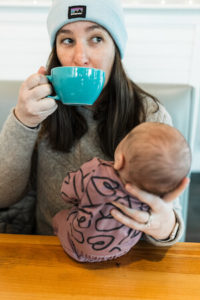 Woman sipping coffee and holding a newborn baby