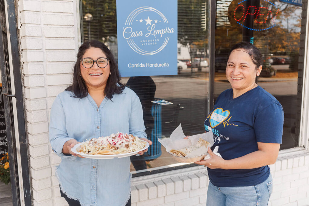 Mary and Eda outside their restaurant, holding plates of food