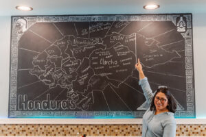 Mary pointing at a map of Honduras on the wall