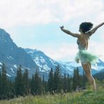 A woman jumping in a field, with a mountain backdrop