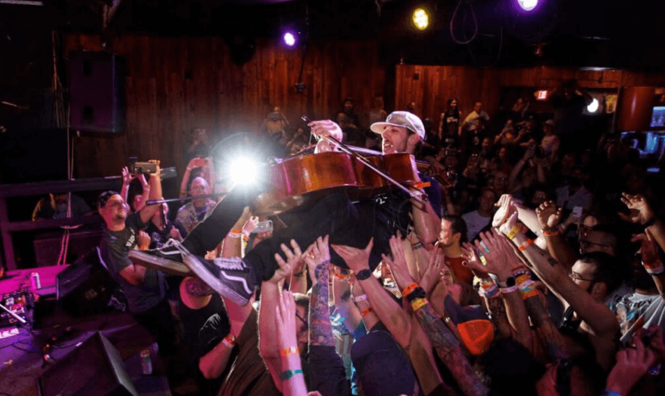 Cellist, playing above a crowd with hands raised