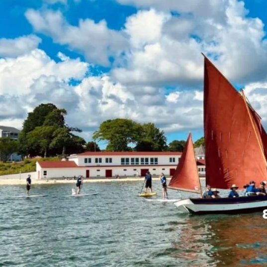 Sailboat with red sail in front of the Onset Bay Center