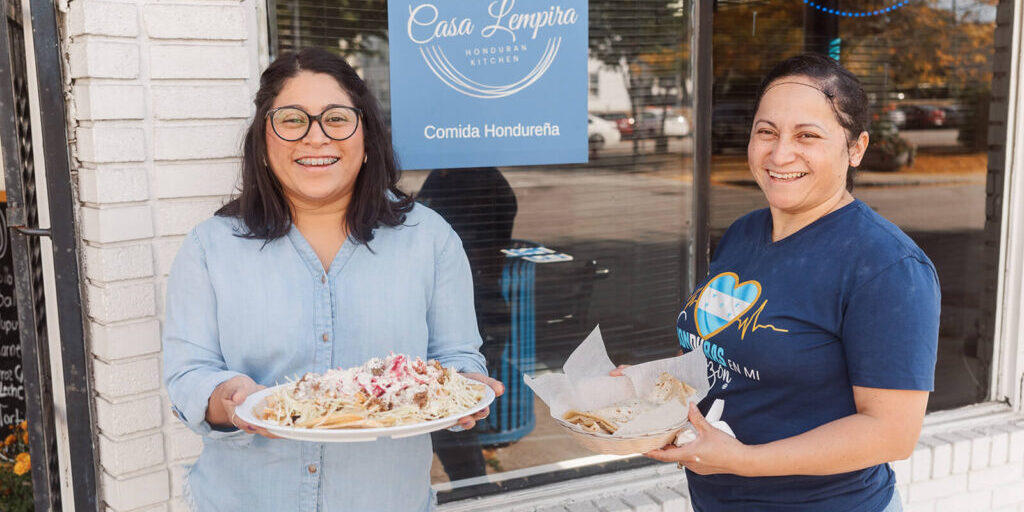 Mary and Eda outside their restaurant, holding plates of food