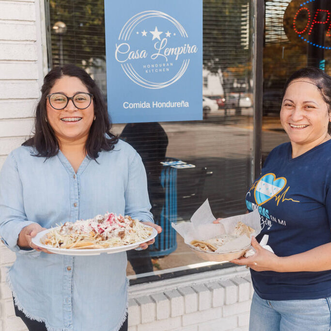 Mary and Eda outside their restaurant, holding plates of food