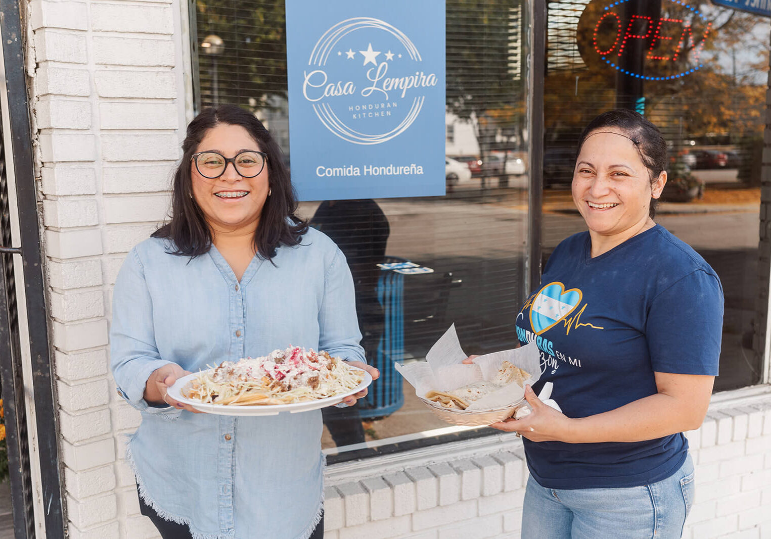 Mary and Eda outside their restaurant, holding plates of food